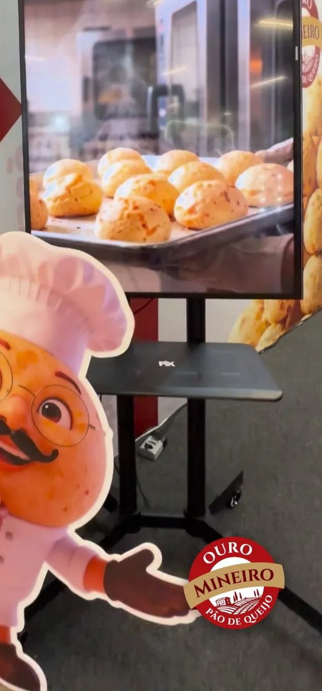 Estande da Ouro Mineiro na feira Encatho, com o display do mascote Dom Queijote ao lado de uma bandeja de pães de queijo.