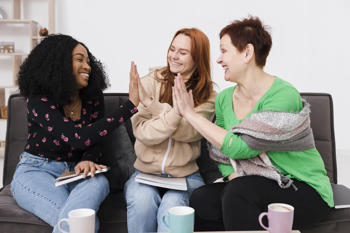 Roda de mulheres conversando numa sala branca e iluminada, com plantas, poltrona de vime e luz natural.